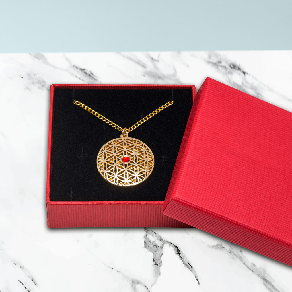 Der Anhänger Blume des Lebens mit rotem Stein wird mit einer Gliederkette in einem Schmuckkästchen verschickt.