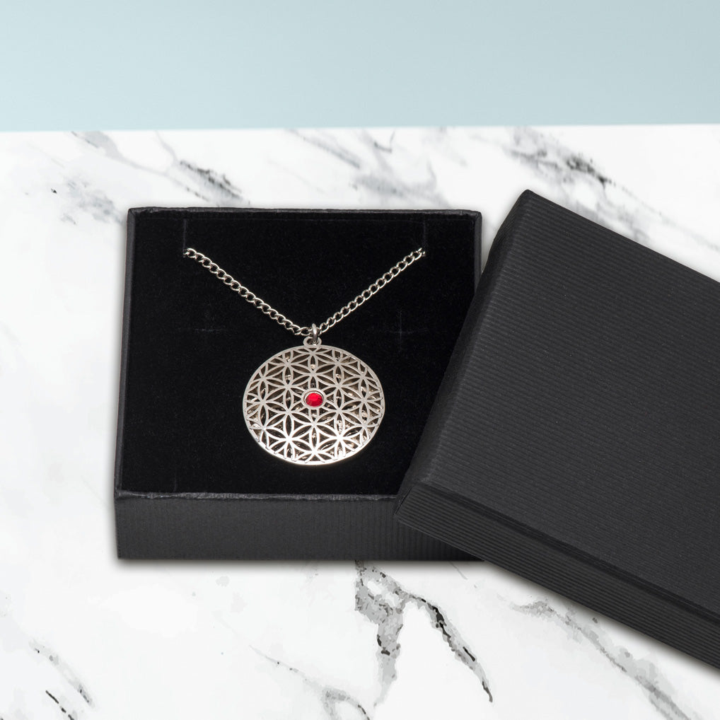 Der Anhänger Blume des Lebens mit rotem Stein wird mit einer Gliederkette in einem Schmuckkästchen verschickt.